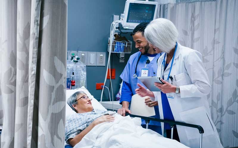 Médico y enfermera hablando con mujer paciente en cama de hospital de urgencias